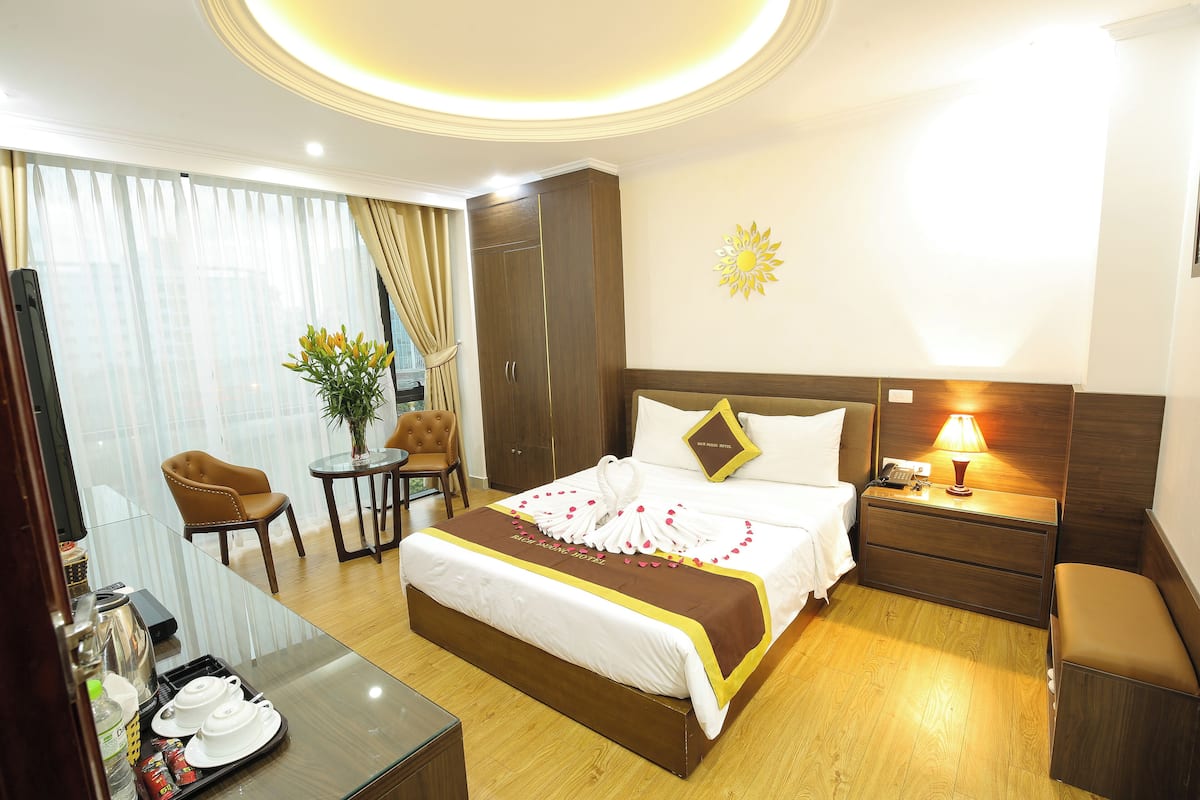 A hotel room with a bed, bedside table, lamp, and a small table with a chair.