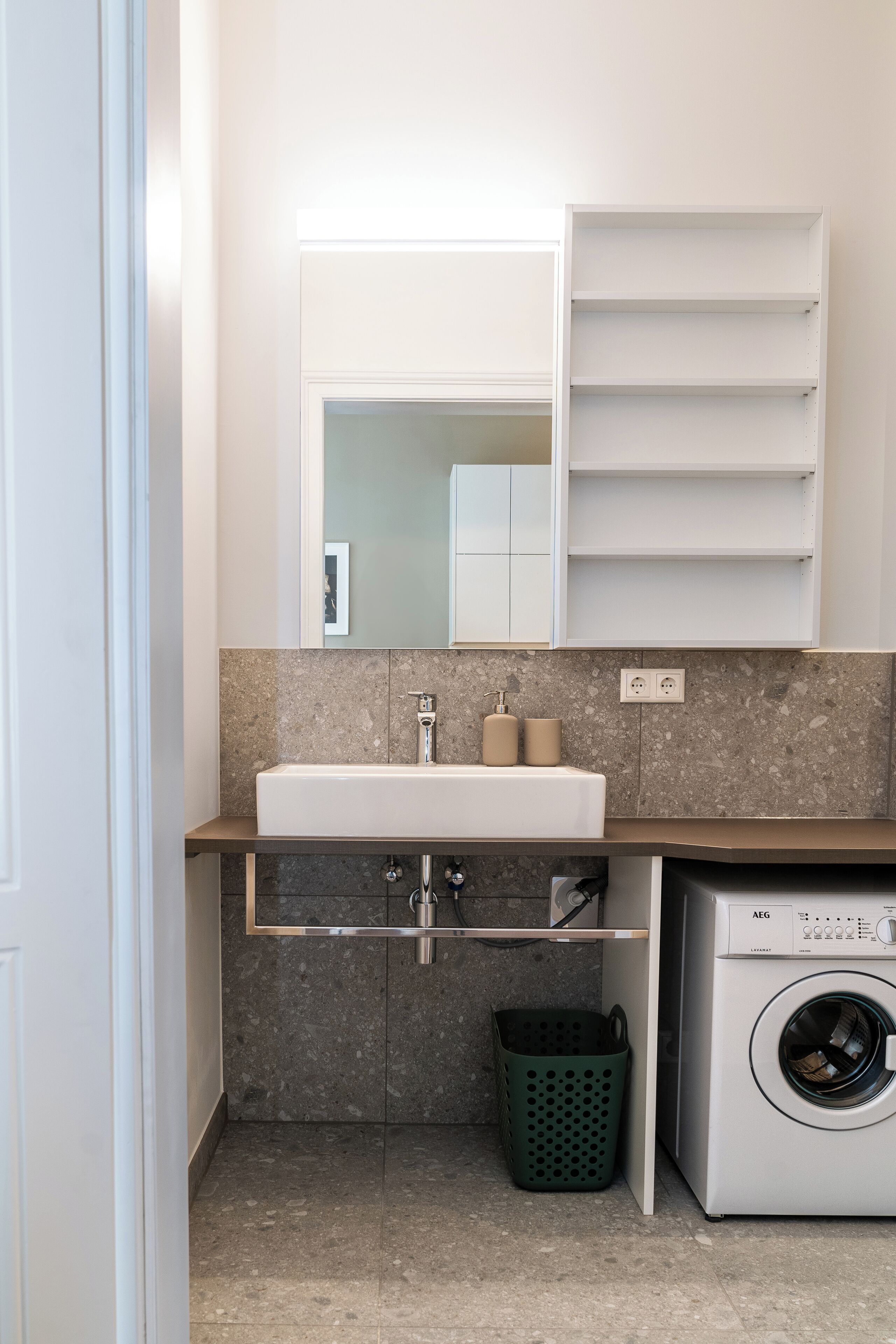 Une petite salle de bain comprenant un lavabo, un miroir, un porte-serviettes et un lave-linge.