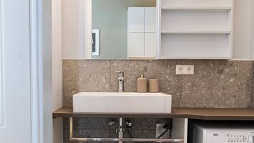 Une petite salle de bain comprenant un lavabo, un miroir, un porte-serviettes et un lave-linge.