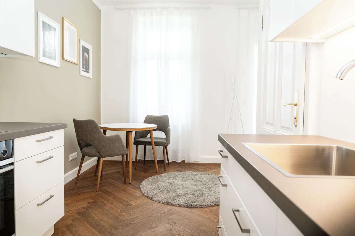 A modern kitchen with a stainless steel sink, wooden cabinets, and a round dining table with chairs.