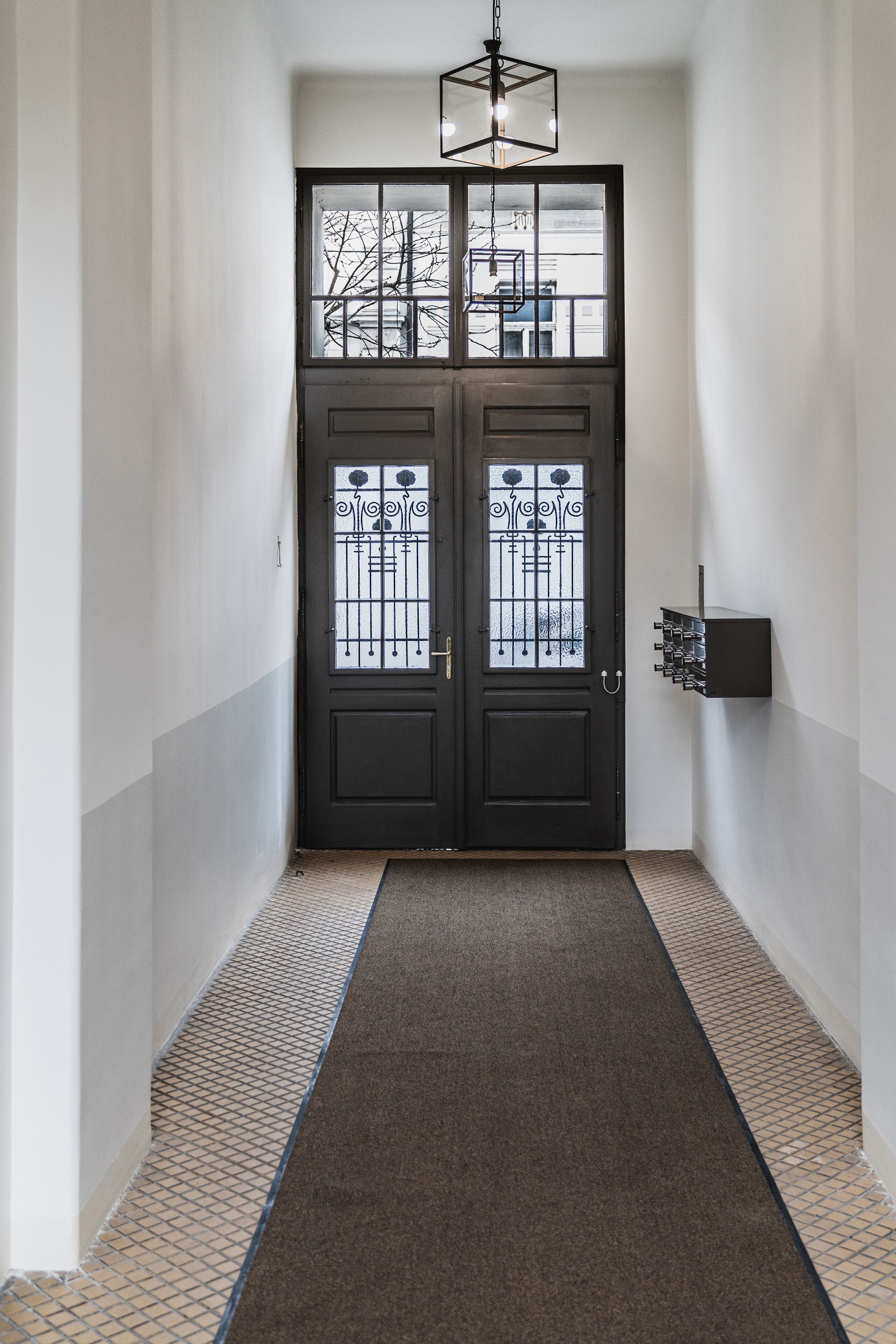 A hallway with a dark double door, a patterned carpet, and a wall-mounted light fixture.