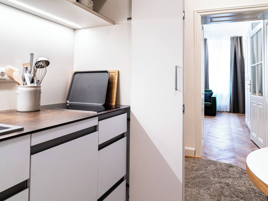 A modern kitchen with a laptop, a coffee maker, and utensils on the counter.