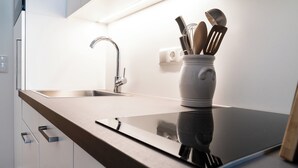 Una cucina moderna con lavello in acciaio inossidabile, un vaso bianco con utensili da cucina e un piano cottura a induzione nero e elegante.
