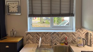 A kitchen with a window, a sink, a dish rack, a kettle, and a clock on the wall. - Cozy Apartment in Stoke-on-trent One Double bed (Stoke-on-Trent)