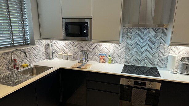 A modern kitchen with a herringbone-patterned backsplash, stainless steel appliances, and black cabinetry. - Cozy Apartment in Stoke-on-trent One Double bed (Stoke-on-Trent)