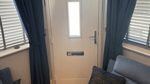 A room with a white door, a window with blinds, a grey sofa, and a dark curtain. - Cozy Apartment in Stoke-on-trent One Double bed (Stoke-on-Trent)