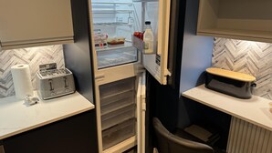 A compact kitchenette with a toaster, a bread box, and a refrigerator with a glass door. - Cozy Apartment in Stoke-on-trent One Double bed (Stoke-on-Trent)