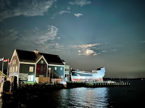 A waterfront building with a dock extending into the water, featuring a large boat. - The Stonehouse Makers' Maisonette (Pictou)