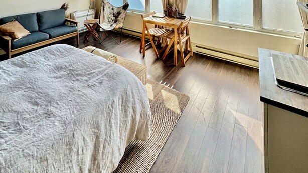 A modern hotel room with a large bed, a sofa, a dining table, and a view of the sea.
