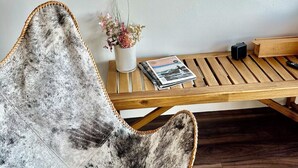A room with a rustic chair, a wooden table, a vase with flowers, and a magazine.