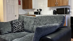 A living room with a grey sofa, a black armchair, and a wooden door. - Flexible One Bedroom Apartment With Sofa Beds (Colchester)