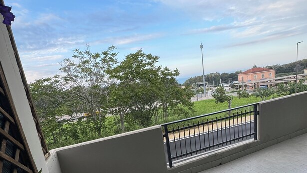 A balcony with a view of a road and buildings, a black chair, a small table with a potted plant, and potted flowers. - Cozy apartment within walking distance of the sea, with pets allowed  (Scalo Ferroviario)