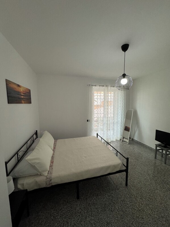 Une chambre à coucher avec un lit, une télévision, un tableau et une fenêtre avec des rideaux.