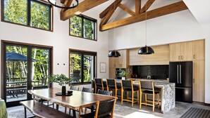 Une cuisine moderne avec des meubles en bois, un réfrigérateur noir et un coin repas comprenant une table et des chaises en bois.