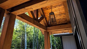 Une structure de plafond en bois, agrémentée d’une lanterne suspendue, et offrant une vue sur une zone boisée.