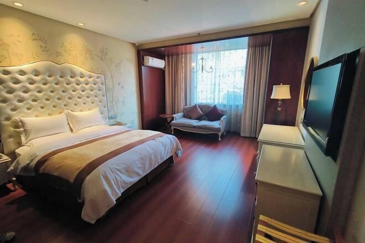 A hotel room with a large bed, a television, a desk, and a window with curtains.