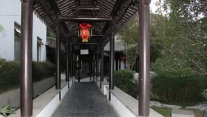 A covered walkway with a tiled floor, surrounded by greenery and a building in the background. - Yangzhou Slender West Lake Huijin Hotel (Yangzhou)