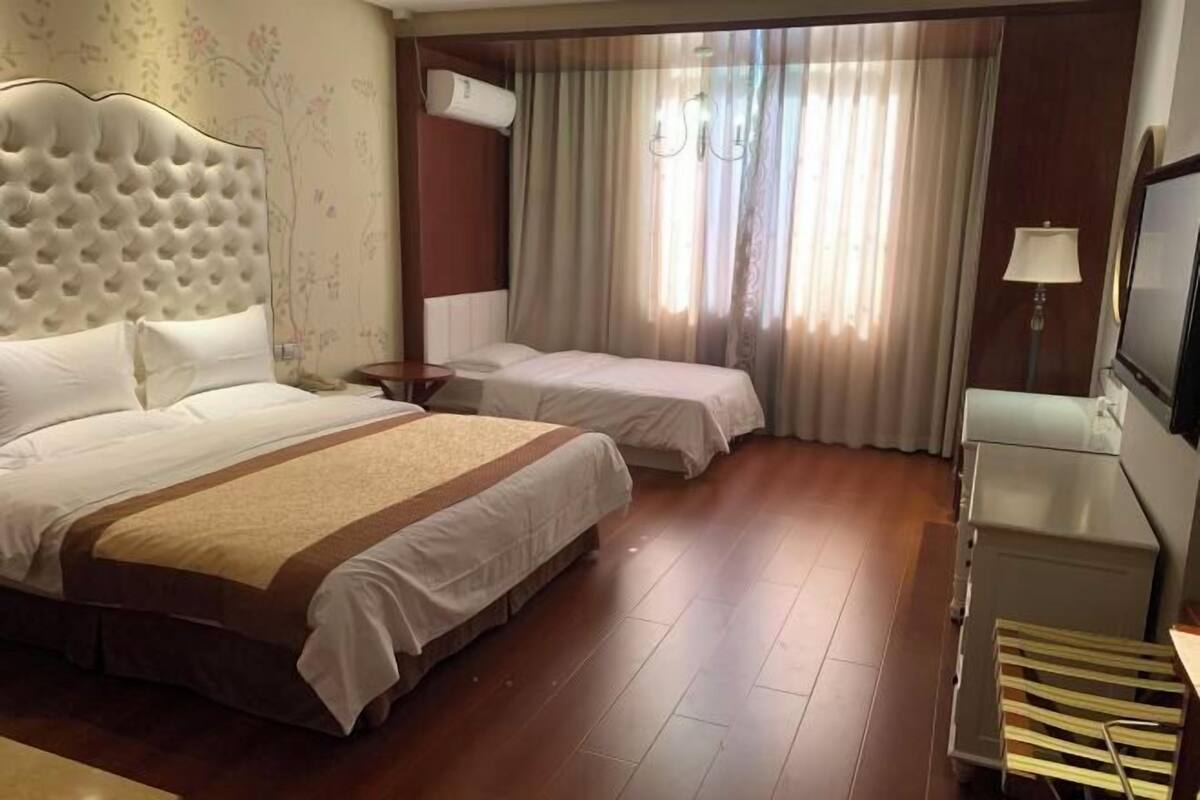 A hotel room with two beds, a TV, a lamp, and a wooden floor.