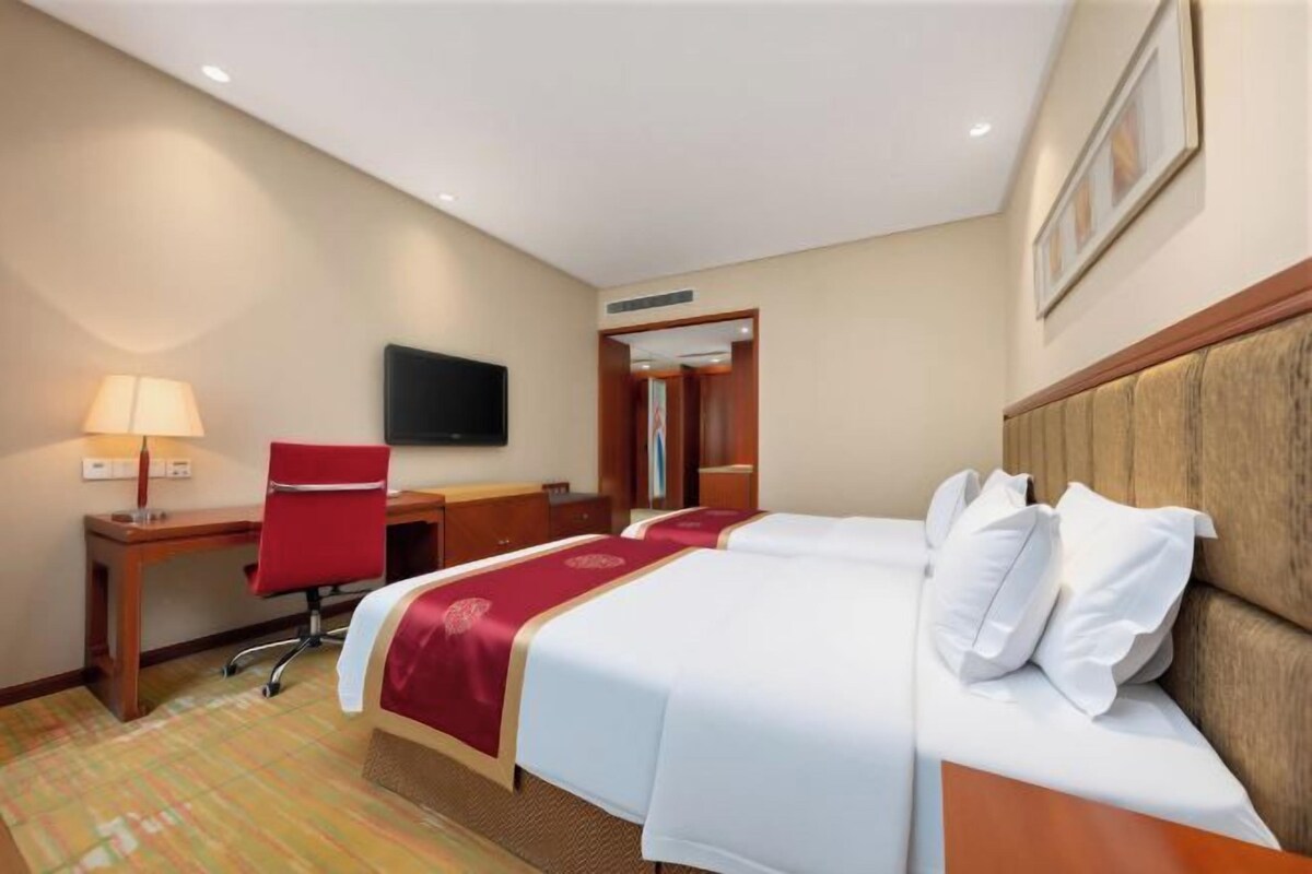 Una habitación de hotel con cama, escritorio, silla, televisor y puerta.
