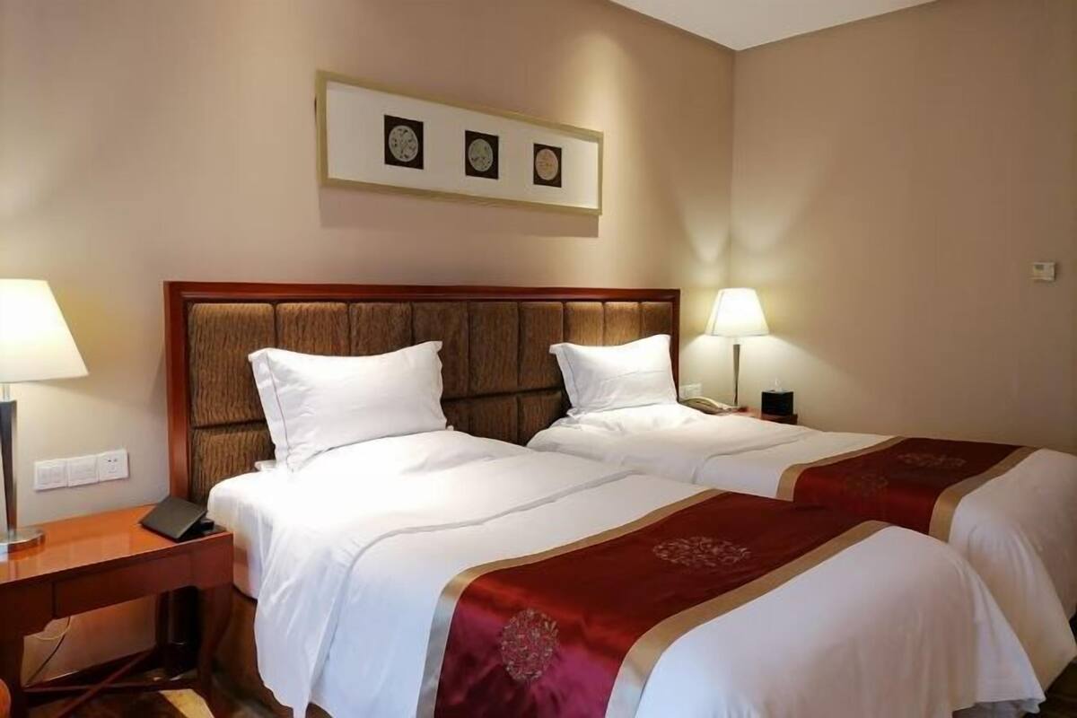 A hotel room with two beds, a wooden headboard, bedside lamps, a desk, and a framed picture on the wall.