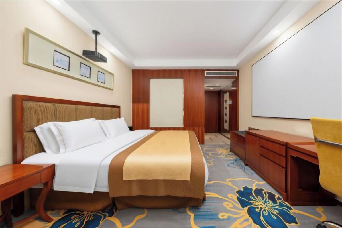 Een hotelkamer met een bed, een bureau, een stoel, een televisie en een deur naar een andere kamer.