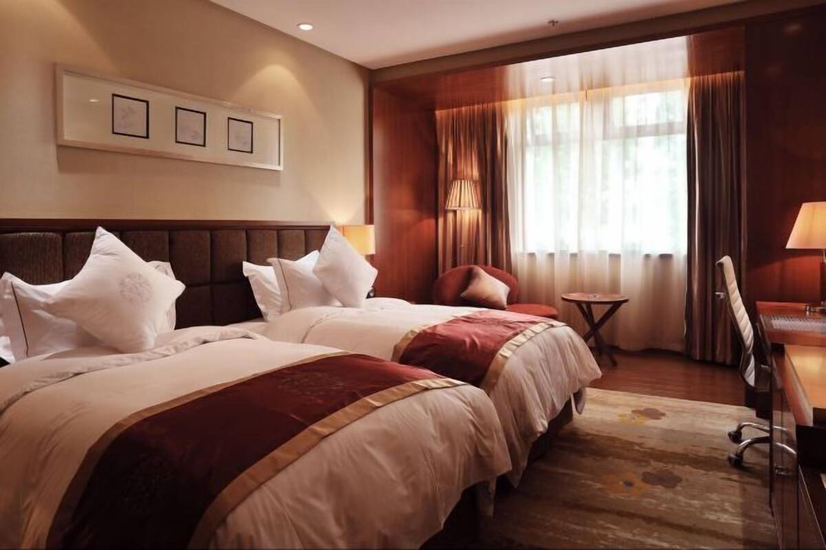 A hotel room with two beds, a small table, a chair, and a desk.