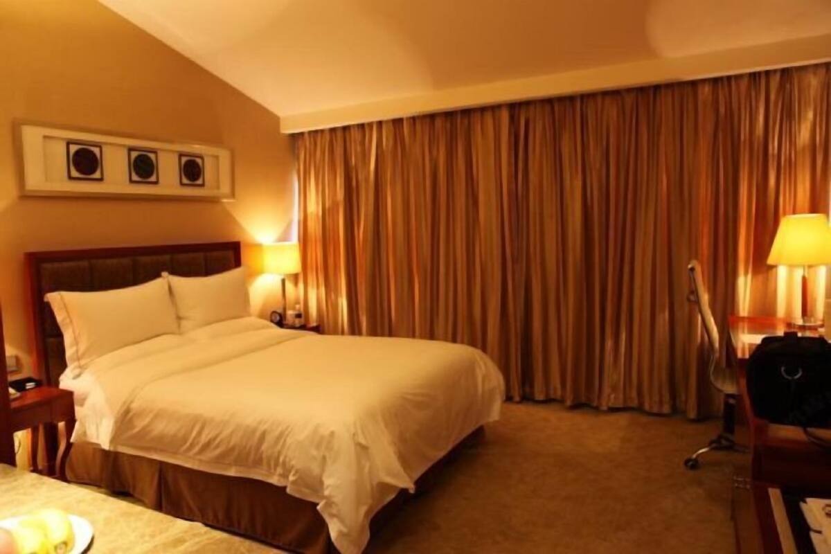 A hotel room with a large bed, two bedside lamps, a desk with a chair, and a curtain backdrop.