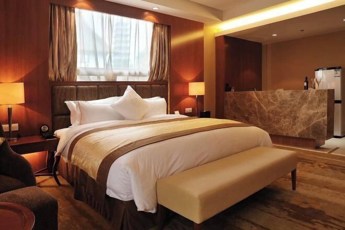 A hotel room with a large bed, a bench, a desk, and a minibar.