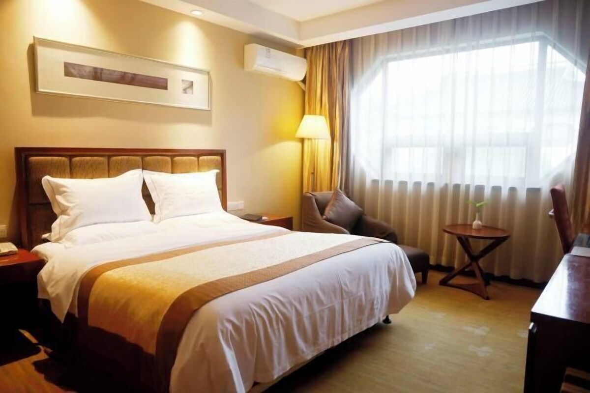 Een hotelkamer met een groot bed, een stoel, een bijzettafeltje en een raam met gordijnen.