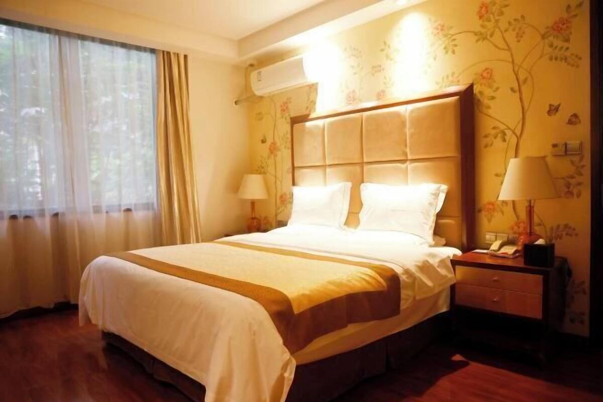 A hotel room with a large bed, a nightstand, a lamp, and a window with curtains.