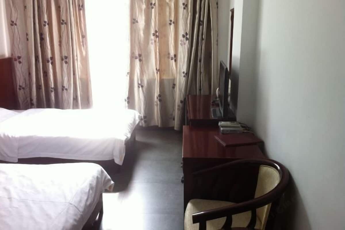 A hotel room with two beds, a desk with a chair, and a window with curtains.