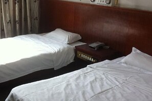 Ein Hotelzimmer mit zwei Betten, einem Holzkopfstück, einem Nachttisch mit Telefon und einem Vorhang mit Blumenmuster.
