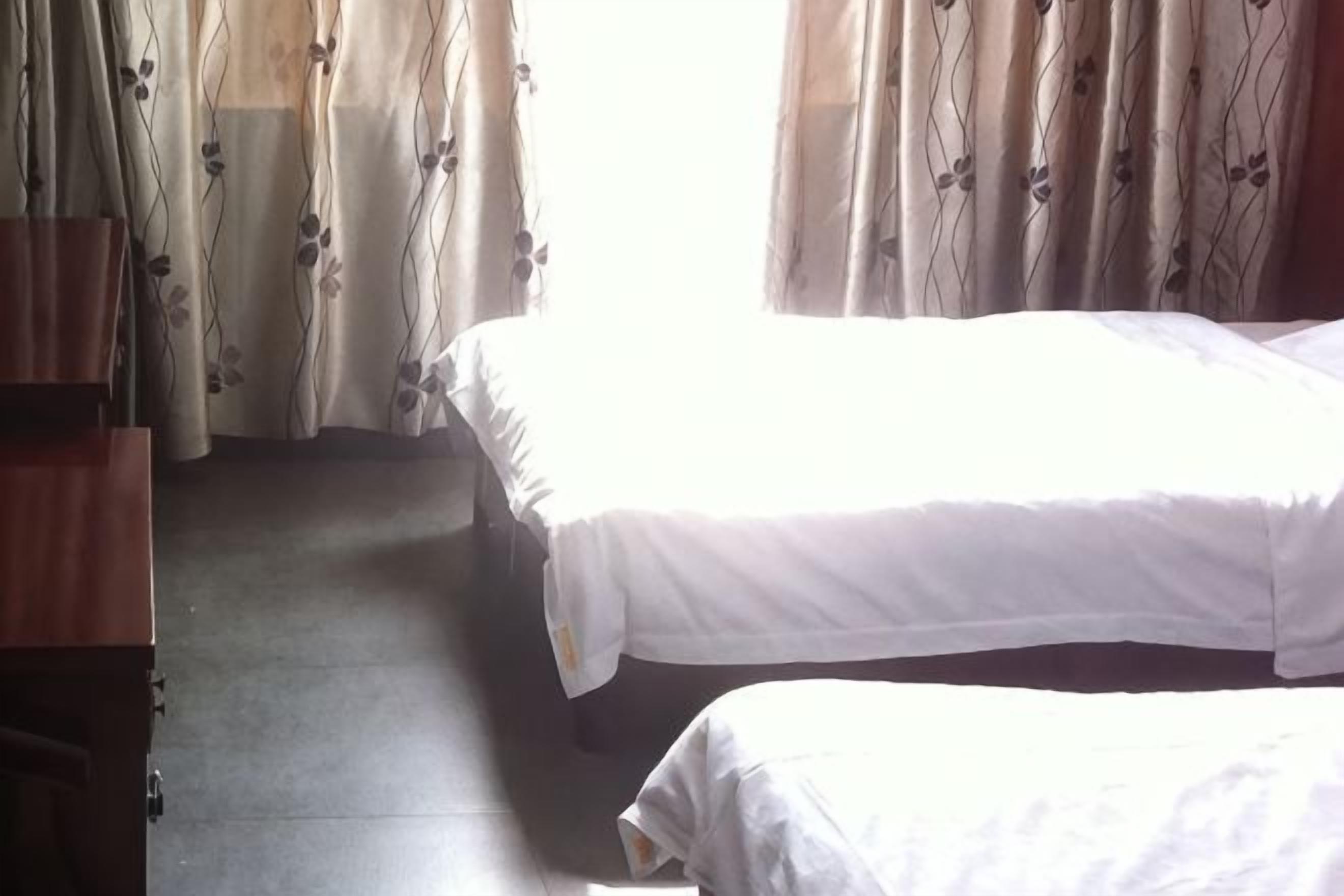 A room with two beds, a wooden wardrobe, and curtains with a floral pattern.