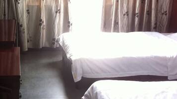 A room with two beds, a wooden wardrobe, and curtains with a floral pattern.
