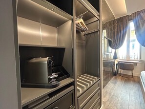 Ein modernes, kompaktes Zimmer mit integriertem Kleiderschrank, einer kleinen Küchenzeile mit Kaffeemaschine und Blick durch ein mit Vorhängen versehenes Fenster nach außen.