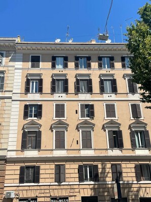 Ein mehrgeschossiges Gebäude mit einheitlicher Fassade, zahlreichen Fenstern mit Rollläden und Satellitenschüsseln auf dem Dach.