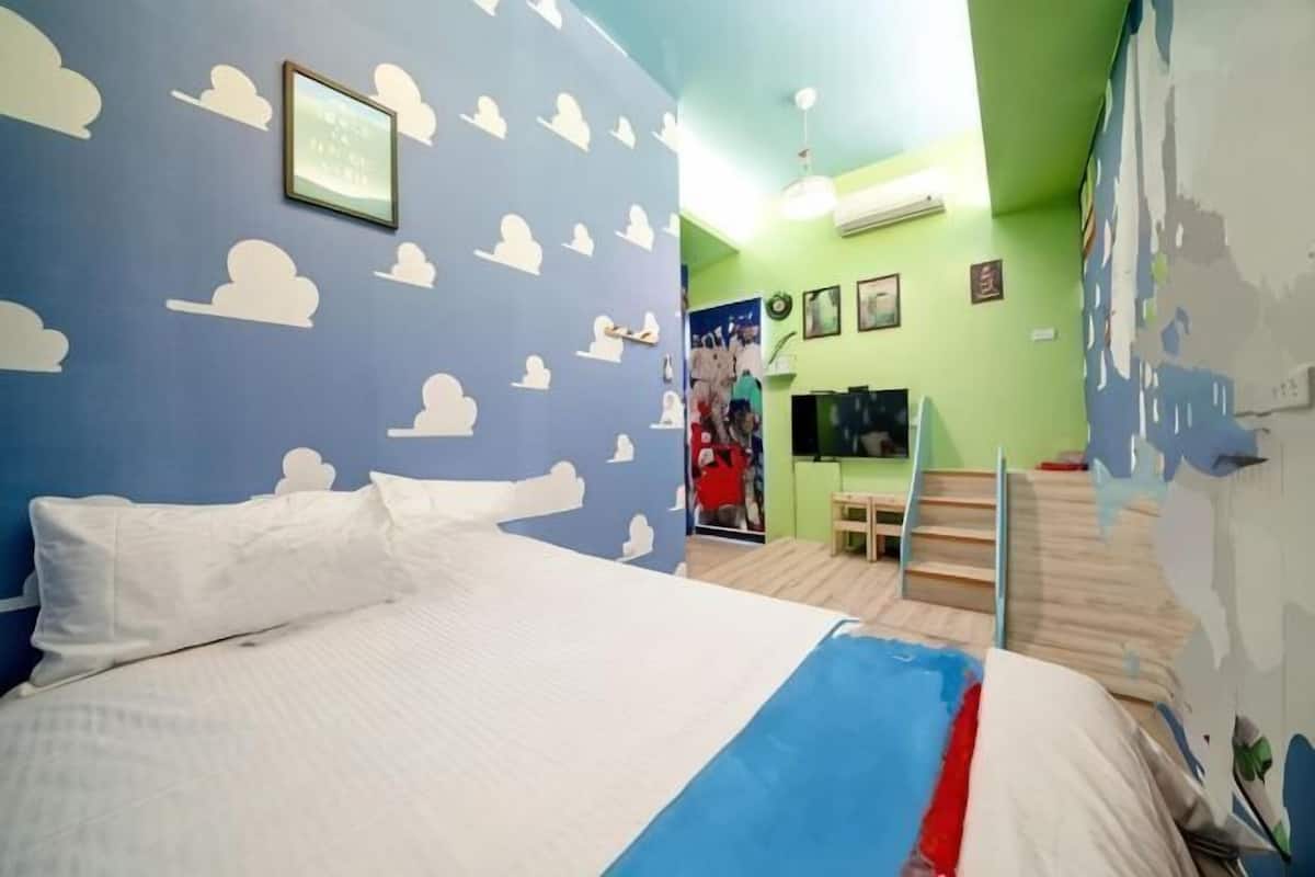 A room with a bed, a TV, a staircase, and a wall with cloud patterns.
