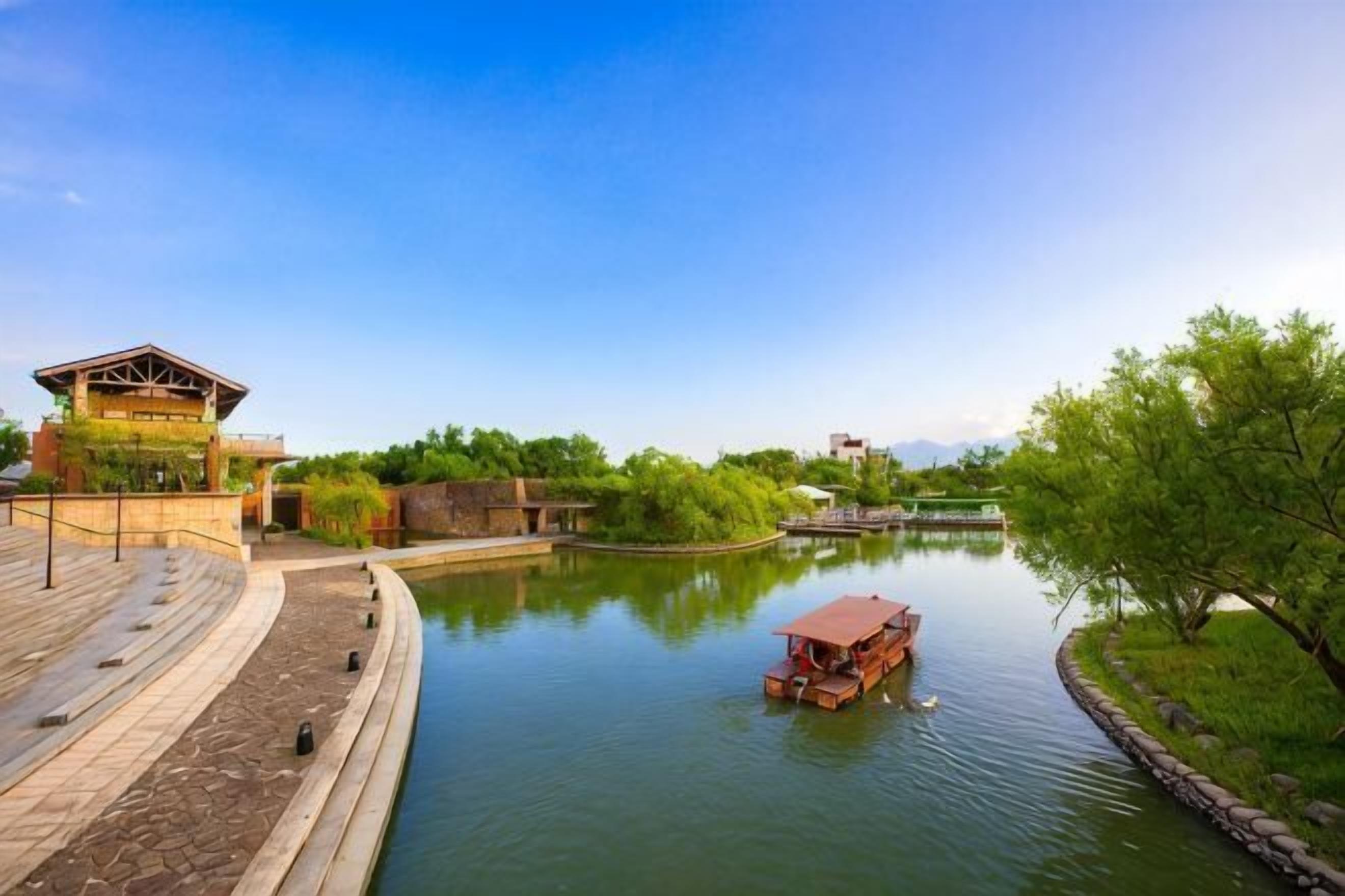 A river with a boat, a wooden dock, and a building with a sloped roof.