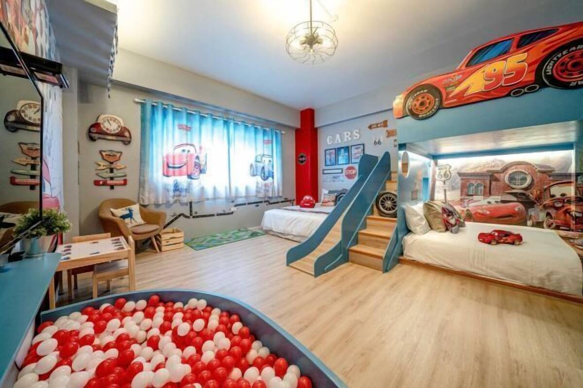 A child's bedroom with a play area, a bed with a car-themed headboard, and a wall decorated with car stickers.