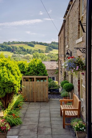 A courtyard with a wooden bench, a stone wall, and a view of the countryside.