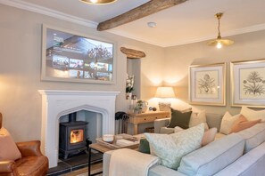 A cozy living room with a fireplace, a comfortable sofa, a television mounted on the wall, and framed botanical artwork on the wall.