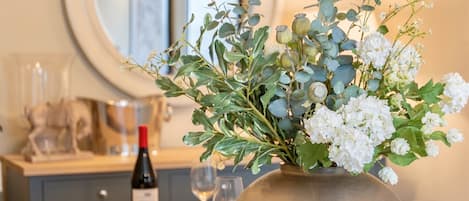 A dining table set with white plates, glasses, and a vase of flowers.