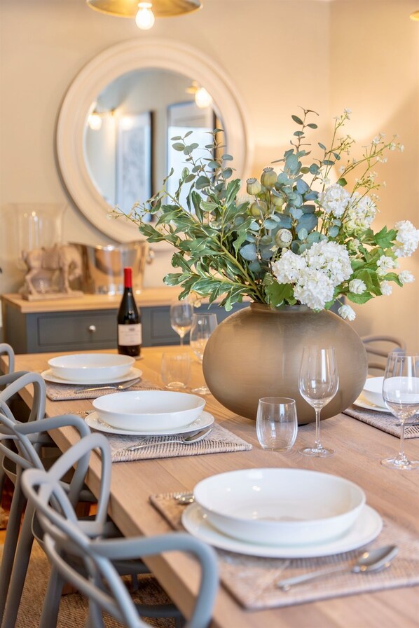 A dining table set with white plates, glasses, and a vase of flowers.