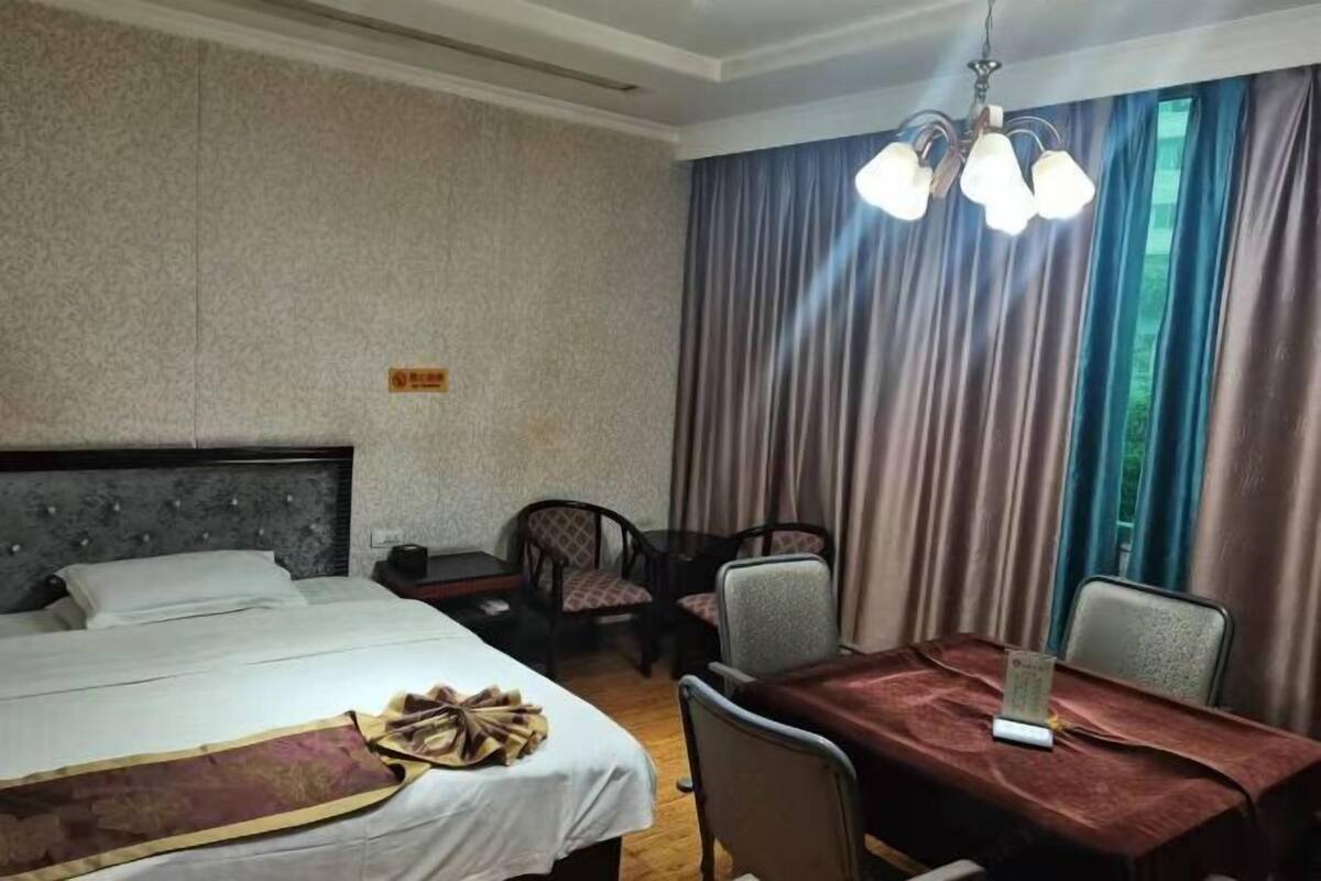 Una habitación de hotel con cama, una mesa de comedor, sillas, una araña y cortinas.