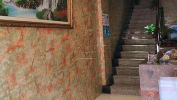 A marble wall with a framed painting, a staircase, and a reception desk.