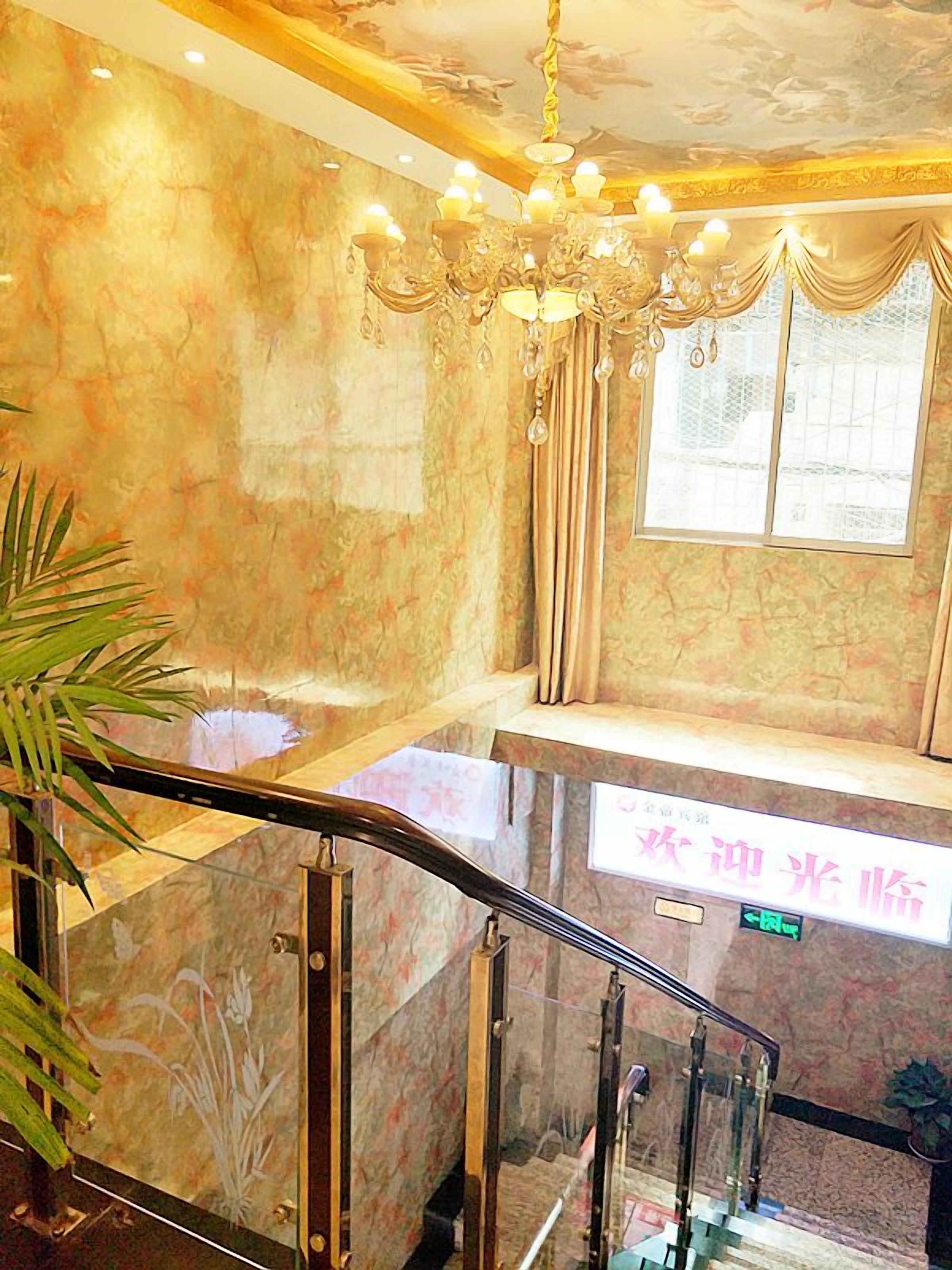 A marble staircase with a glass railing, a chandelier, and a window with curtains.