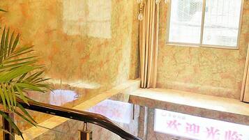 A marble staircase with a glass railing, a chandelier, and a window with curtains.