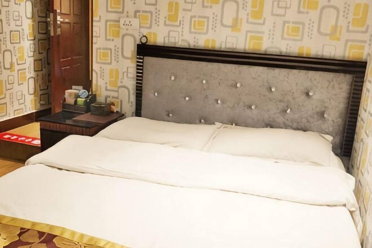 Una cama bien hecha con cabecera, una mesita de noche con lámpara y papel tapiz estampado.