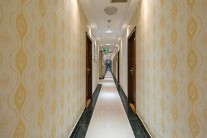 Un pasillo largo y estrecho con papel tapiz estampado y suelo brillante, que conduce a una puerta al final.