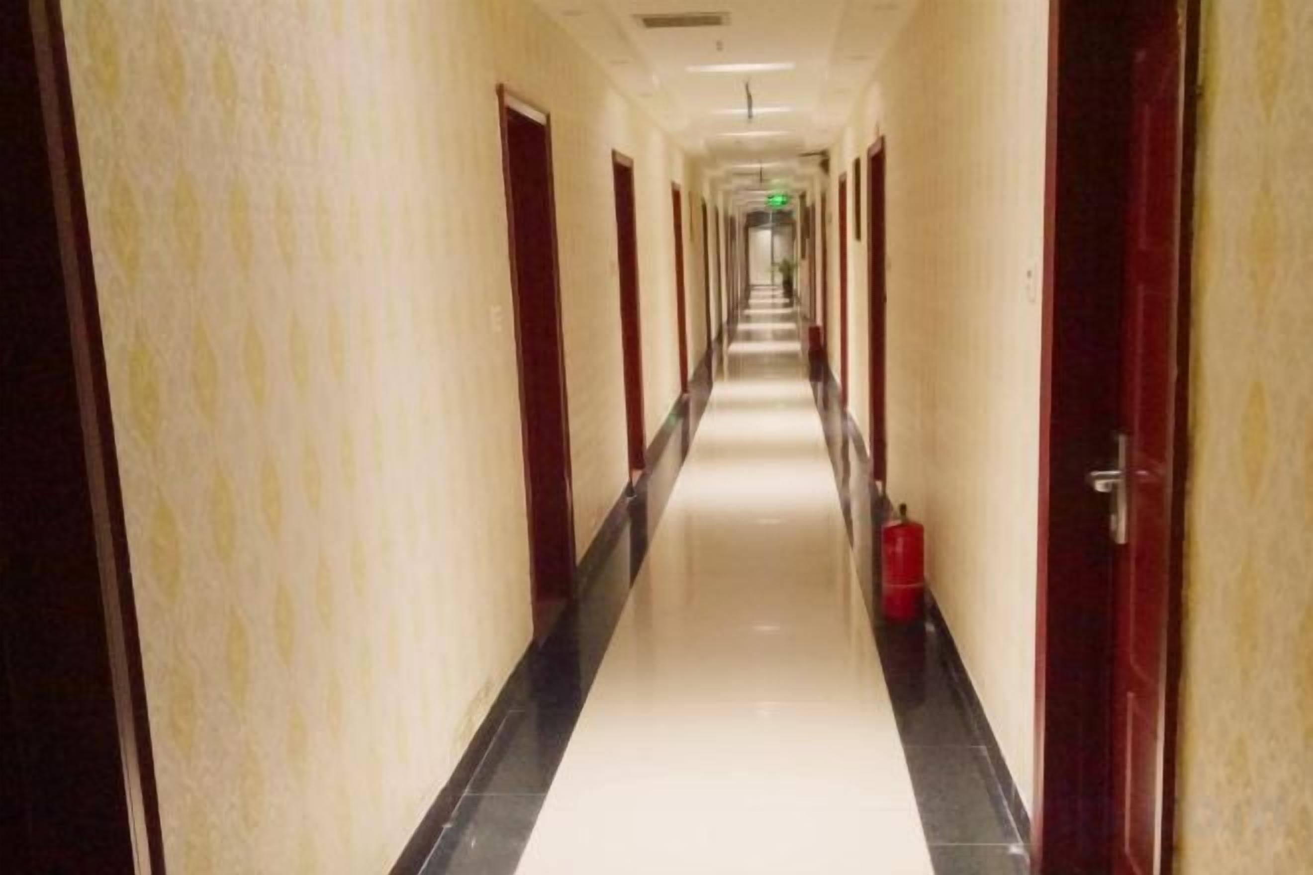 A long, narrow hotel corridor with doors on both sides and a red fire extinguisher on the right.